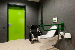 a toilet for disabled people with green bars, wheelchair and door