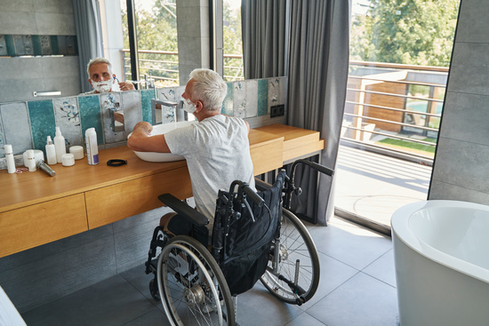 Aging man wheelchair user looking in mirror and moving razor blade along his cheek